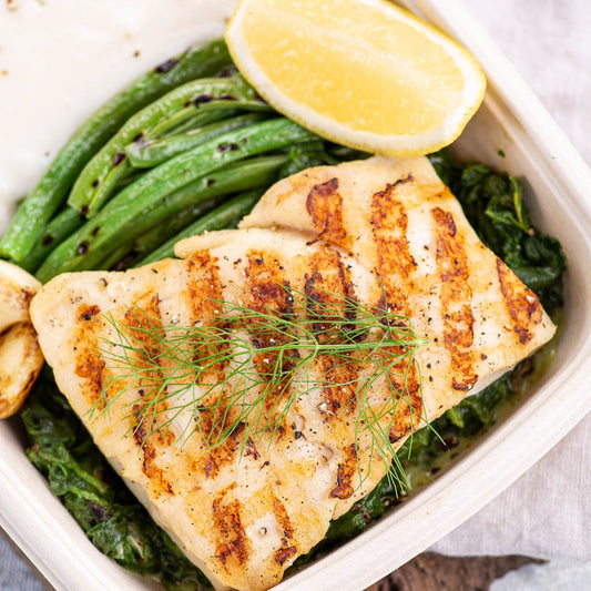 A prepared Keto meal Plan consisting of grilled fish and green vegetables, served in a white container with a lemon wedge on the side.
