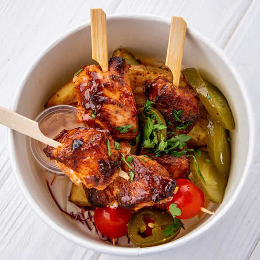 A bowl of meal skewers with chicken, tomatoes, and bell peppers, garnished with herbs.