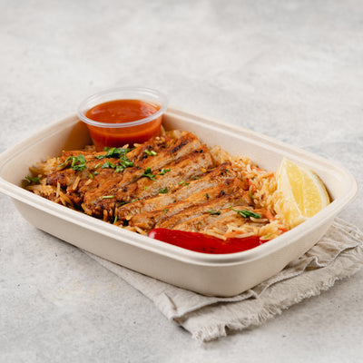 A prepared meal in a white take-out container, garnished with a lemon slice and accompanied by a small dish of sauce. Meal Plan for busy individual.