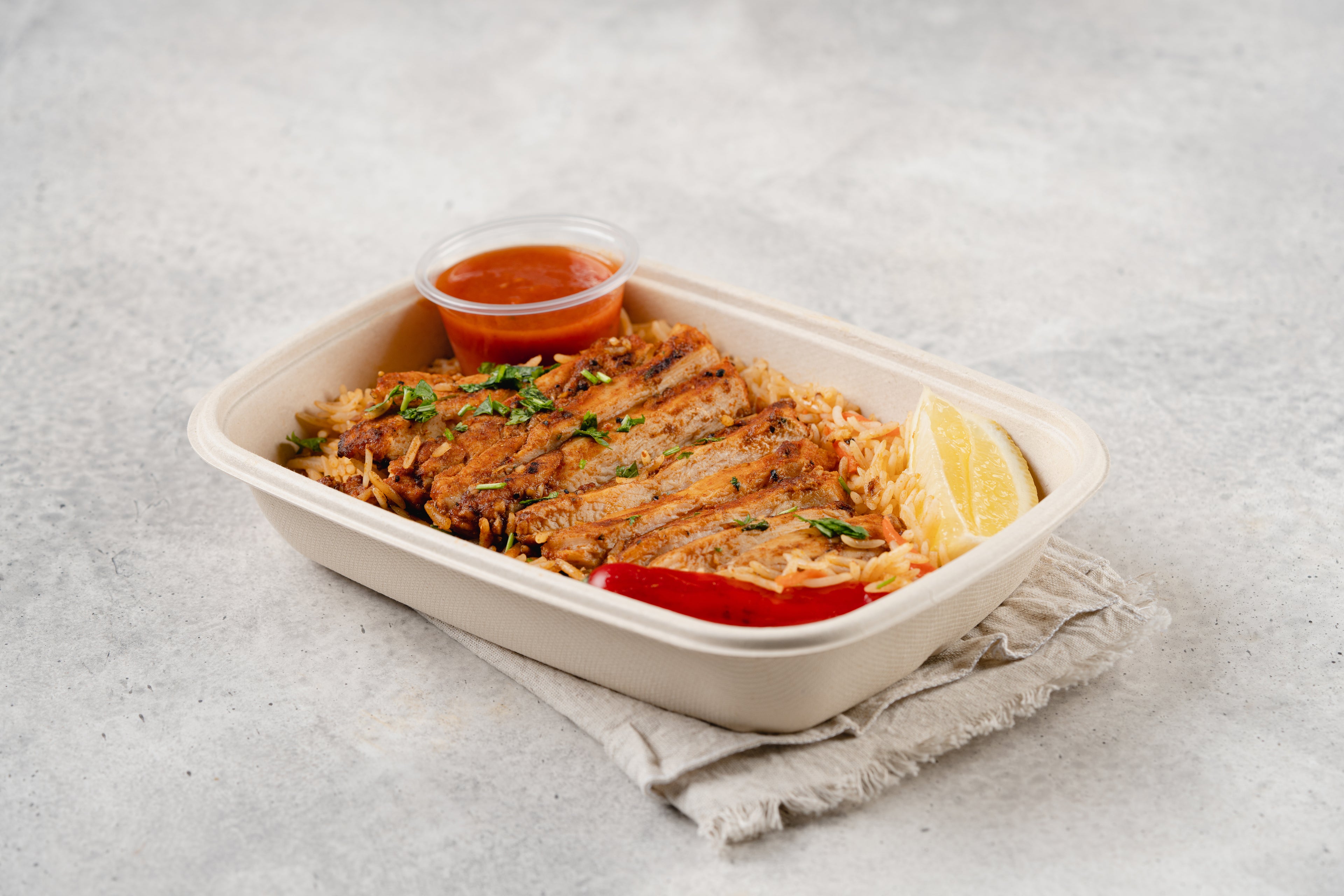 A prepared meal in a white take-out container, garnished with a lemon slice and accompanied by a small dish of sauce. Meal Plan for busy individual.
